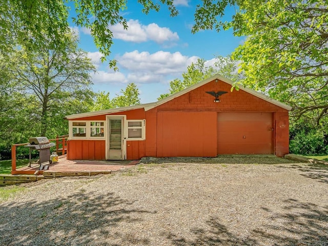 view of front of home with a wooden deck, gravel driveway, a detached garage, and an outdoor structure