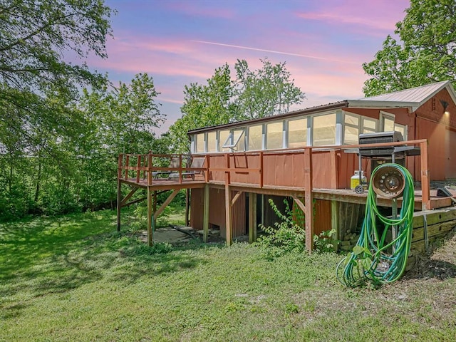 back of house at dusk with a deck, stairs, a lawn, and metal roof