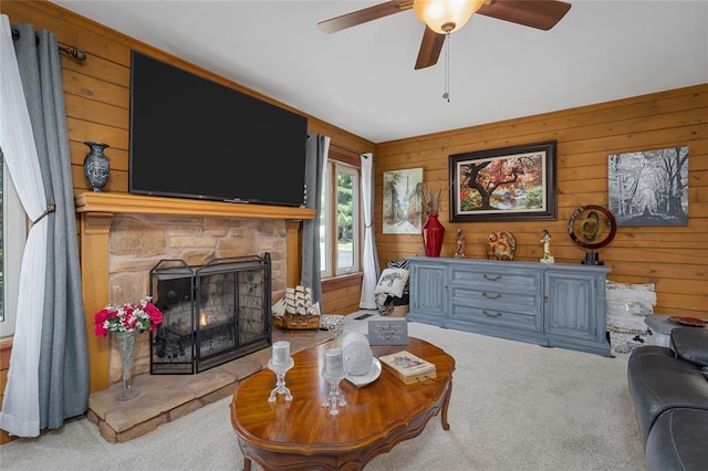 carpeted living area featuring wooden walls, a ceiling fan, and a stone fireplace