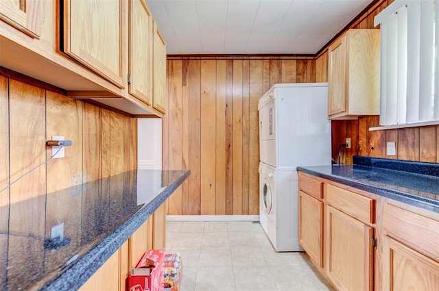 clothes washing area featuring stacked washer and clothes dryer, wood walls, light tile patterned flooring, and cabinet space