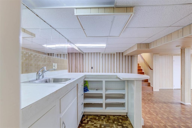 kitchen featuring a sink, a drop ceiling, light countertops, a peninsula, and white cabinets