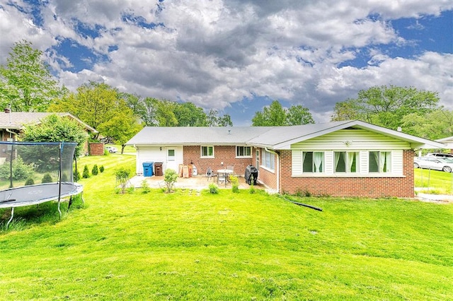 rear view of house featuring a patio area, a trampoline, a yard, and brick siding