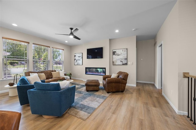 living area with wood finished floors, a ceiling fan, a glass covered fireplace, baseboards, and recessed lighting