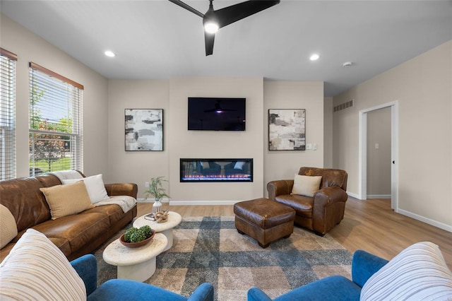 living room with wood finished floors, ceiling fan, baseboards, a glass covered fireplace, and recessed lighting