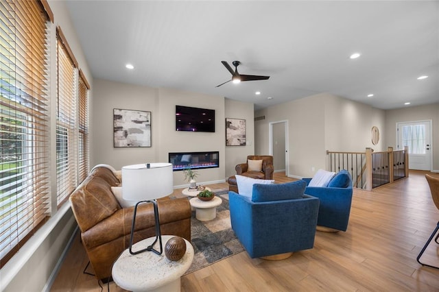 living area with wood finished floors, a ceiling fan, a glass covered fireplace, recessed lighting, and baseboards