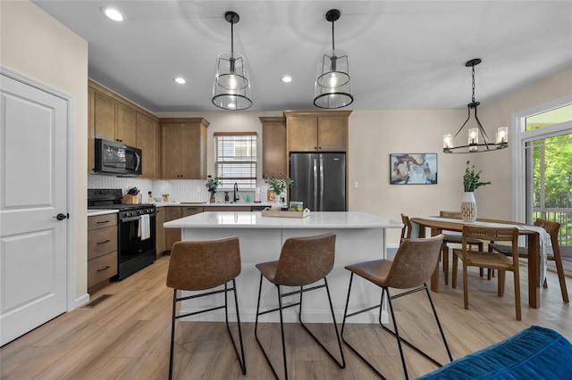 kitchen with black gas stove, freestanding refrigerator, light countertops, a sink, and recessed lighting