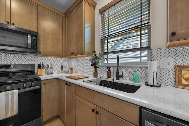 kitchen featuring black gas range oven, a sink, backsplash, stainless steel dishwasher, and light stone counters