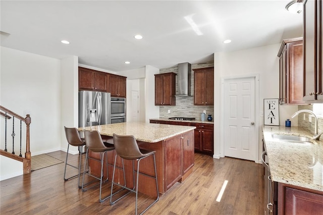 kitchen with appliances with stainless steel finishes, a sink, wall chimney exhaust hood, a center island, and tasteful backsplash