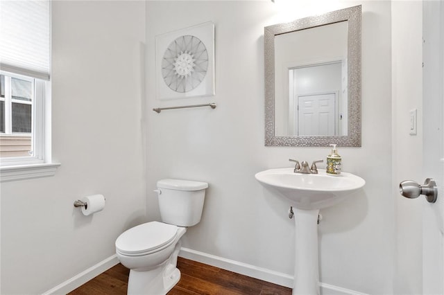 half bathroom with baseboards, toilet, wood finished floors, and a sink