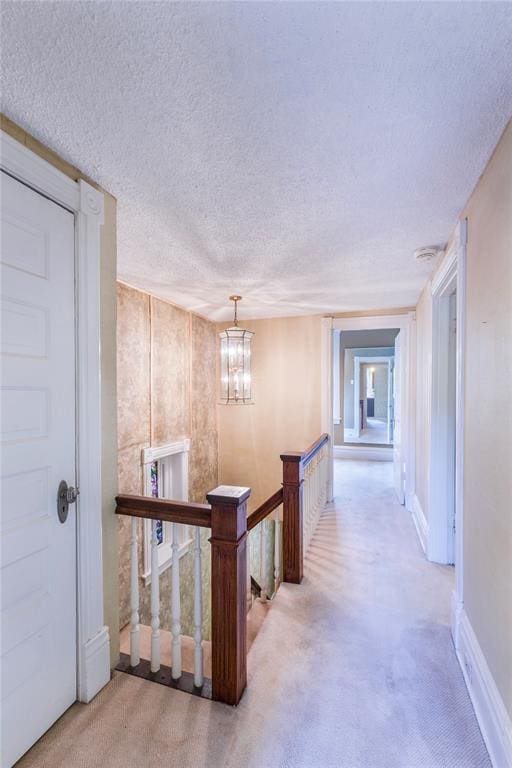 4526 Gibson Ave, Saint Louis, MO 63110 - hallway featuring light carpet, a chandelier, a textured ceiling, an upstairs landing, and baseboards