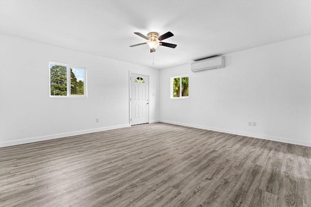 empty room with a wall unit AC, ceiling fan, wood finished floors, and baseboards