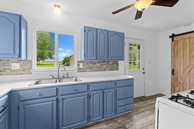 kitchen featuring blue cabinetry, a sink, a barn door, gas range gas stove, and a ceiling fan