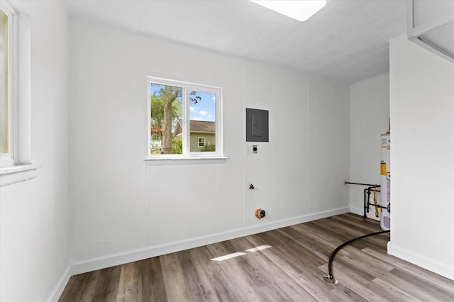 empty room with electric panel, wood finished floors, water heater, and baseboards
