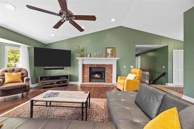 living area with vaulted ceiling, wood finished floors, a ceiling fan, baseboards, and a brick fireplace