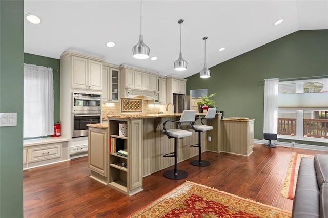 kitchen featuring cream cabinetry, stainless steel appliances, vaulted ceiling, decorative backsplash, and dark wood-type flooring