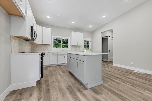 kitchen with a barn door, baseboards, stainless steel microwave, a center island, and decorative backsplash