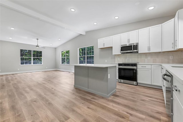 kitchen with appliances with stainless steel finishes, ceiling fan, decorative backsplash, a kitchen island, and light wood-type flooring