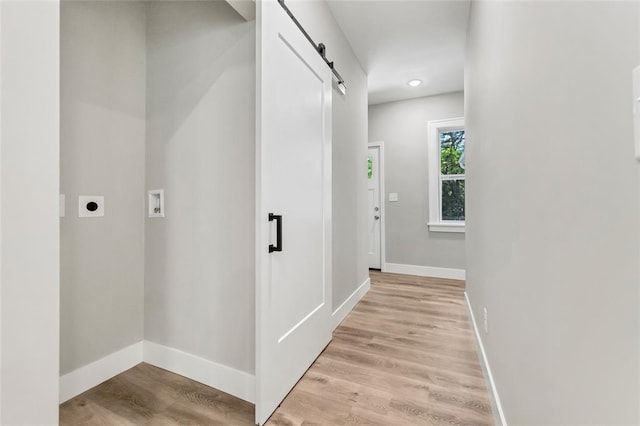 corridor featuring a barn door, baseboards, and light wood-style floors