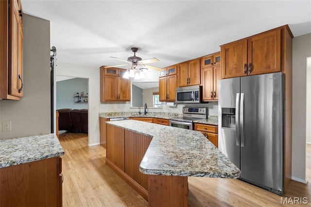 8 Baron Ridge Ct, Ofallon, MO 63366 - kitchen featuring appliances with stainless steel finishes, brown cabinetry, glass insert cabinets, a center island, and light wood-style floors