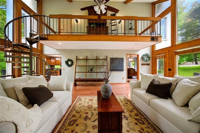 living area with stairs, a high ceiling, a ceiling fan, wood finished floors, and plenty of natural light