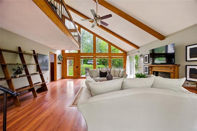 living room featuring high vaulted ceiling, light wood-type flooring, beam ceiling, a fireplace, and a ceiling fan
