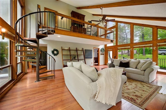 living area featuring stairway, plenty of natural light, a ceiling fan, beam ceiling, and light wood-type flooring