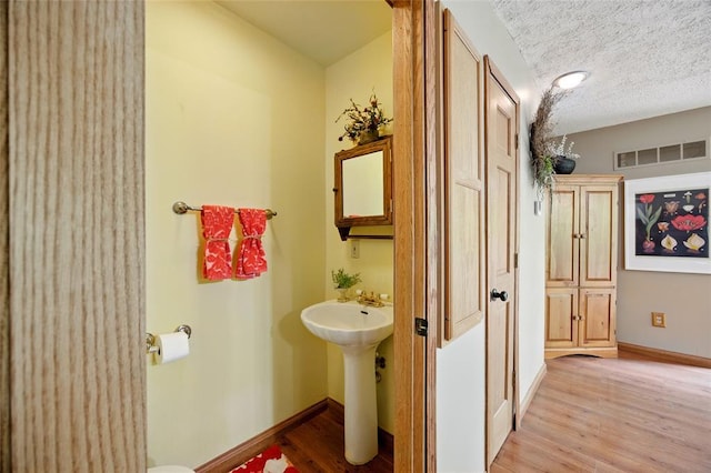 bathroom featuring wood finished floors, baseboards, a textured ceiling, and a sink
