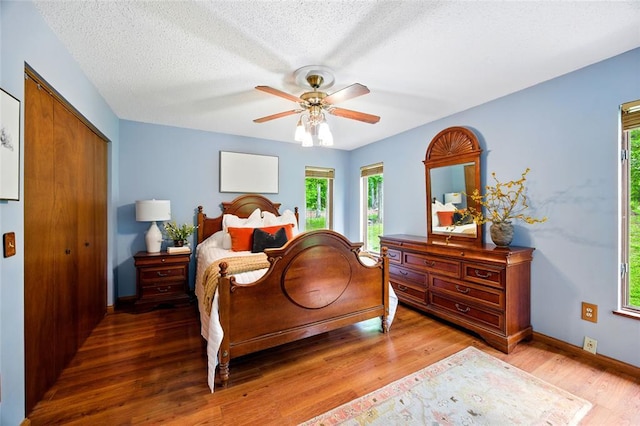 bedroom featuring wood finished floors, a closet, a ceiling fan, baseboards, and a textured ceiling