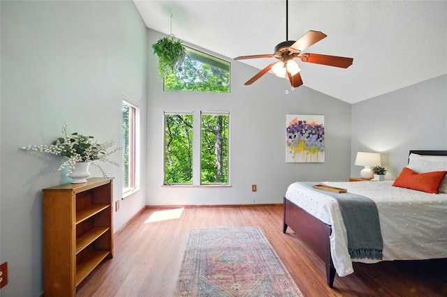 bedroom with light wood-type flooring, high vaulted ceiling, baseboards, and a ceiling fan