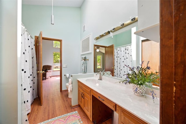 bathroom featuring wood finished floors, a high ceiling, vanity, toilet, and baseboards