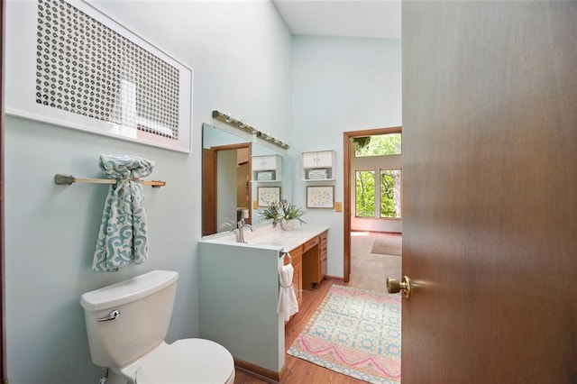 bathroom with a towering ceiling, wood finished floors, toilet, and vanity