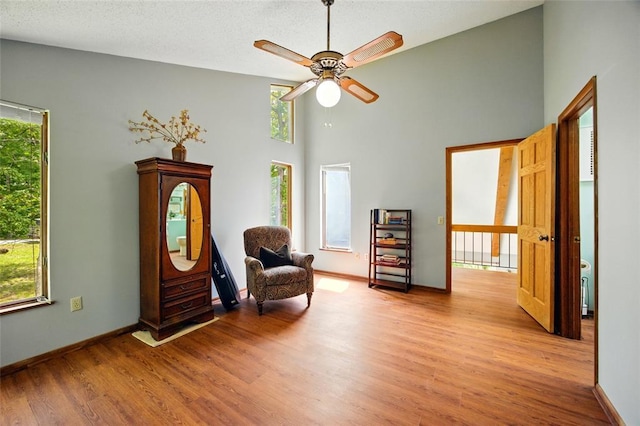 sitting room with wood finished floors, a towering ceiling, a ceiling fan, and baseboards