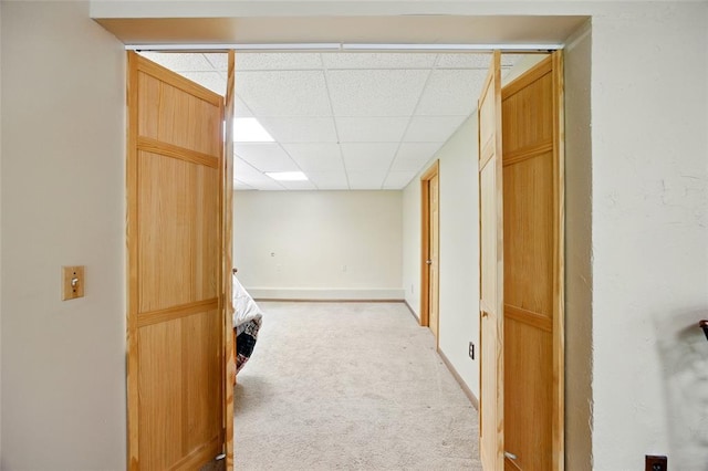 basement featuring a paneled ceiling, light carpet, and baseboards