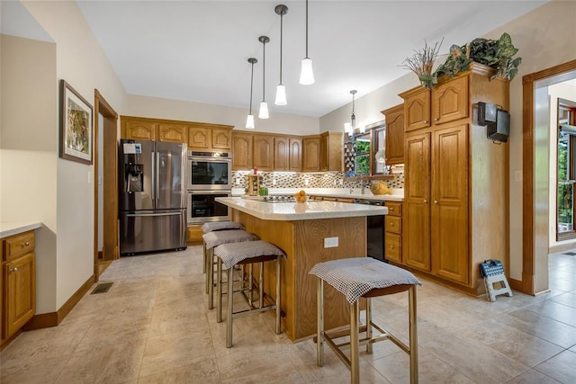 214 Townview Ct, Wentzville, MO 63385 - kitchen with appliances with stainless steel finishes, tasteful backsplash, brown cabinetry, a kitchen island, and light countertops