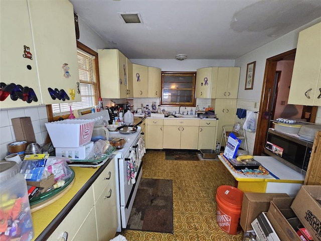 kitchen featuring cream cabinets, white range with electric cooktop, a sink, and stainless steel microwave