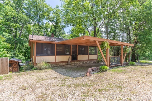 rear view of house featuring a sunroom, a storage unit, an outbuilding, and metal roof