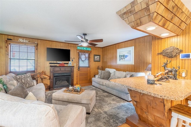 carpeted living area featuring ceiling fan, wood walls, and a glass covered fireplace