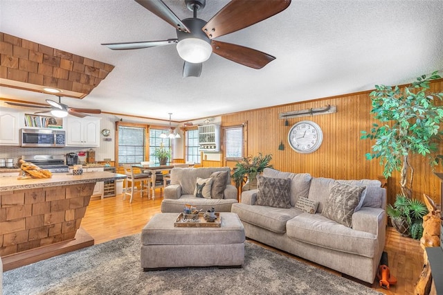 living room with a ceiling fan, a textured ceiling, wood walls, and light wood-style flooring