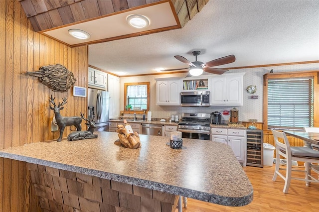 kitchen with appliances with stainless steel finishes, wine cooler, crown molding, white cabinets, and light wood-style flooring