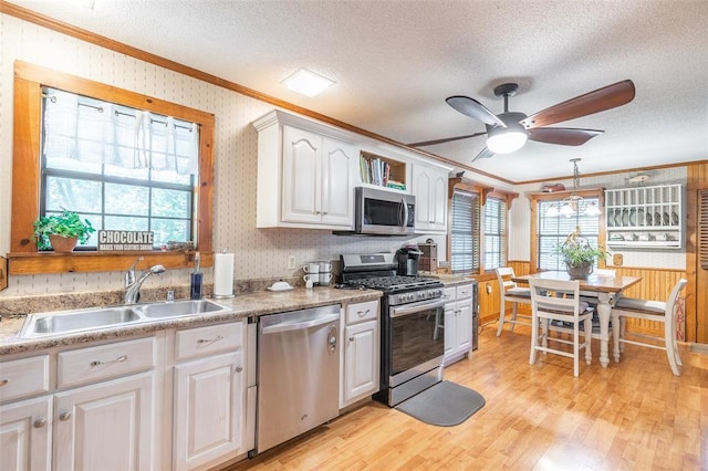 kitchen featuring appliances with stainless steel finishes, crown molding, a sink, a textured ceiling, and light wood-type flooring