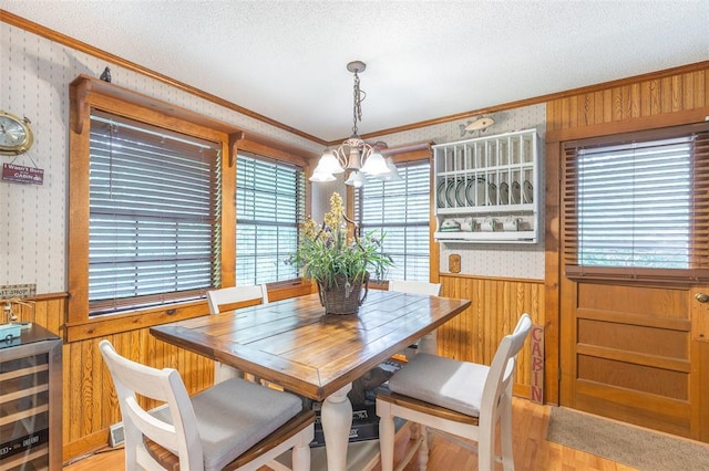 dining area featuring wallpapered walls, crown molding, wine cooler, light wood-type flooring, and a textured ceiling