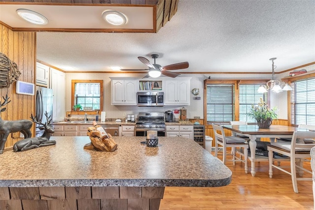 kitchen with appliances with stainless steel finishes, crown molding, light wood finished floors, white cabinets, and a textured ceiling