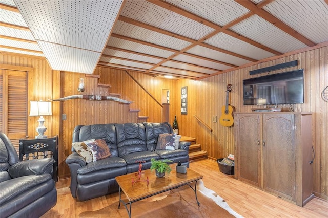 living room with stairs, light wood-style floors, and wooden walls