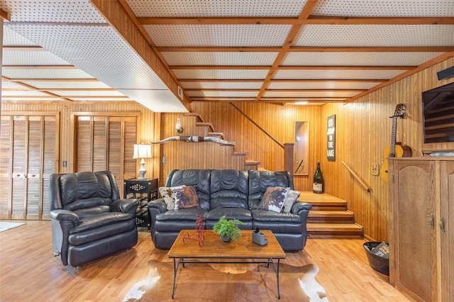 living room with wooden walls, stairway, light wood-style flooring, and beam ceiling