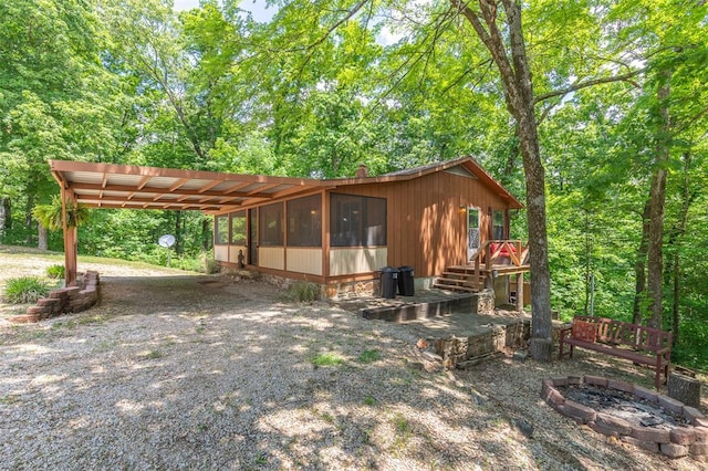 view of front facade with gravel driveway, an attached carport, a fire pit, and a chimney