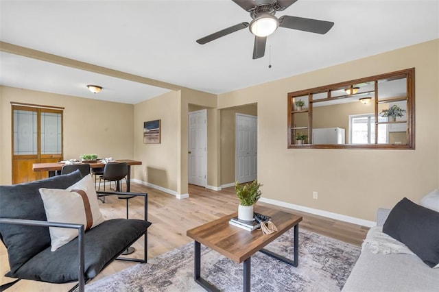 living room featuring baseboards, light wood-type flooring, and a ceiling fan