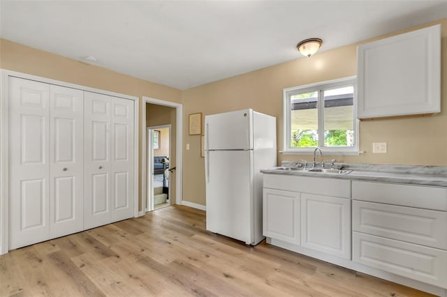 kitchen featuring freestanding refrigerator, a sink, light wood-type flooring, white cabinets, and light countertops