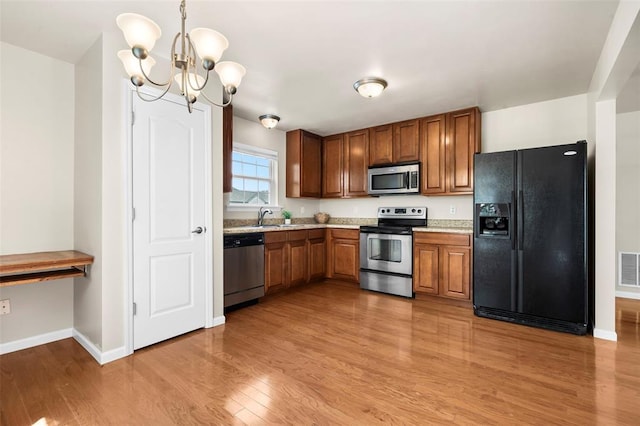 1131 Welsh Dr, Lake St Louis, MO 63367 - kitchen featuring appliances with stainless steel finishes, a chandelier, light wood-style floors, baseboards, and brown cabinets