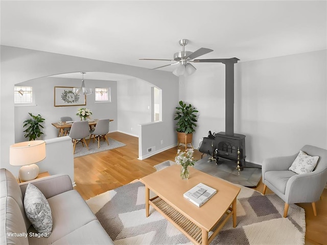 6504 Hoffman Ave, Saint Louis, MO 63139 - living room with arched walkways, light wood-style flooring, a ceiling fan, a wood stove, and baseboards