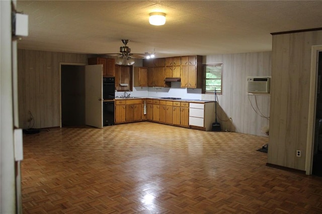 kitchen featuring wooden walls, a ceiling fan, an AC wall unit, light countertops, and brown cabinetry